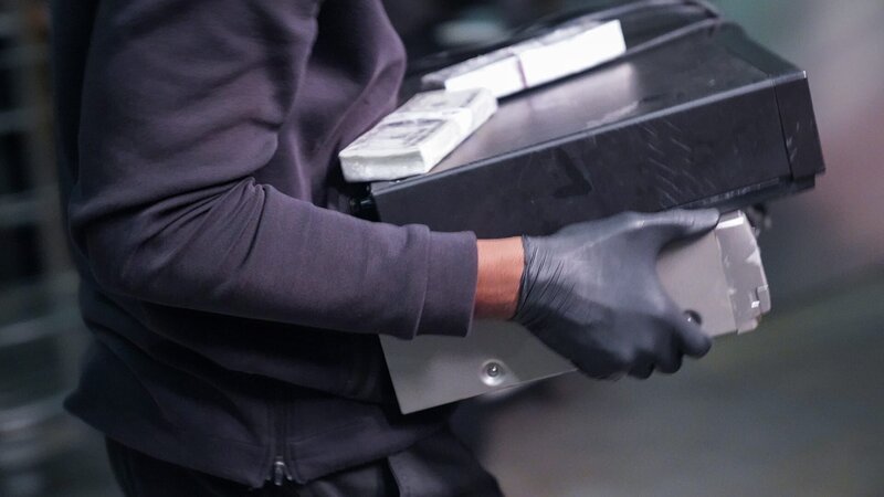 Ein Räuber mit Handschuhen trägt eine Aktentasche und Geld. – Bild: Warner Bros. Discovery