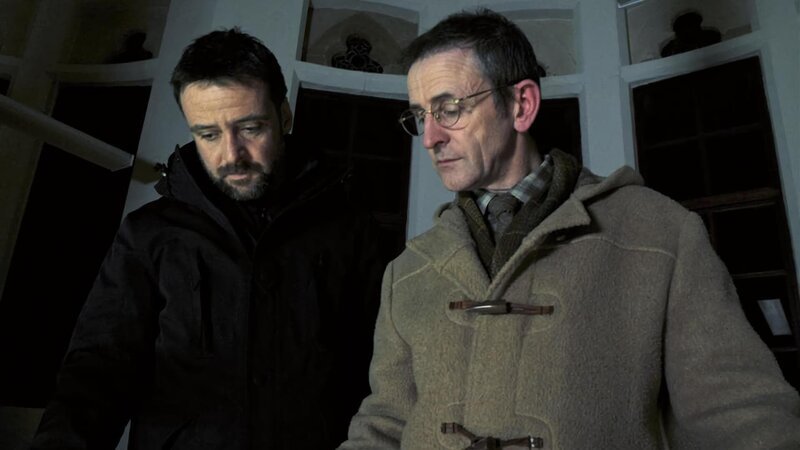 Chief Inspector Tom Mathias (Richard Harrington, li.) lässt sich von dem Gilde-Mitarbeiter Joseph Roberts (Llion Williams) Unterlagen zeigen, die ihm Hinweise in einem Mordfall geben könnten. – Bild: ARD Degeto/​Fiction Factory S4C all3media