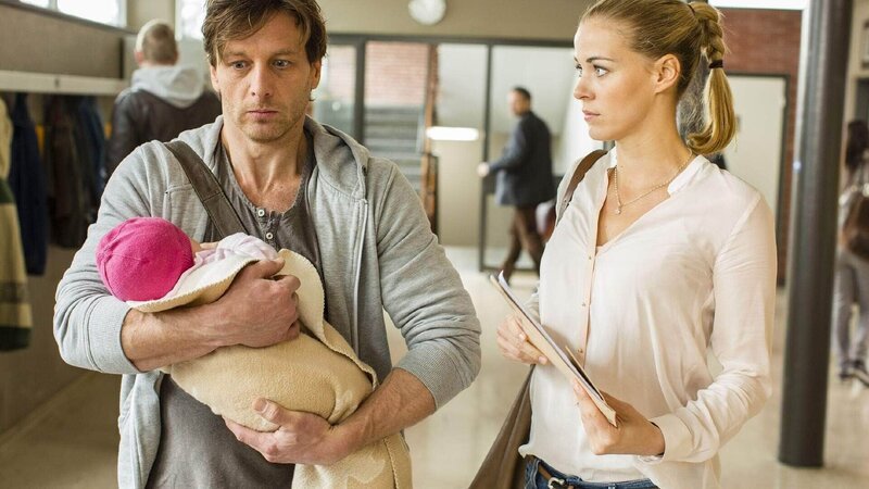 Karin (Jessica Ginkel) ist erstaunt, als sie ihren etwas hilflos wirkenden Kollegen Stefan (Hendrik Duryn) im laufenden Schulbetrieb mit einem Baby auf dem Arm antrifft. – Bild: TVNOW /​ Frank Dicks