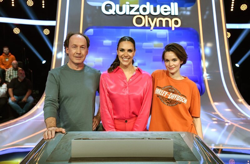 Quizmasterin Esther Sedlaczek (M.) mit den Kandidat:innen des Teams „Ku’damm“: Ulrich Noethen (l.), Schauspieler und Emilia Schüle (r.), Schauspielerin. – Bild: ARD/​Uwe Ernst