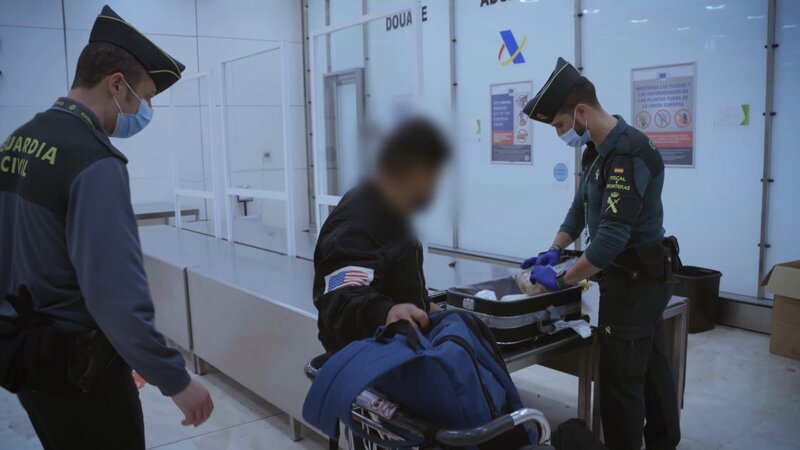 Grenzbeamte kontrollieren den Koffer. – Bild: Warner Bros. Discovery