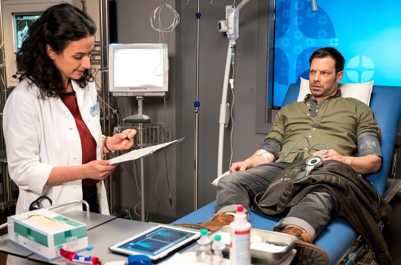 Dr. Sherbaz (Sanam Afrashteh, l.) versorgt den Unfallpatienten Thomas Sommer (Andreas Christ, r.). Dieser interessiert sich nur dafür, wie es seinem Partner Max Krohn geht, der im selben Auto saß. – Bild: ARD/​Jens-Ulrich Koch