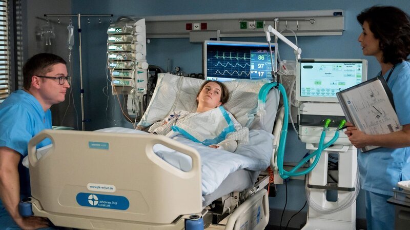 Elias Bähr (Stefan Ruppe, l.) hält Wache am Bett seiner Schwester (Ella-Maria Gollmer, M.) während Prof. Patzelt (Marijam Agischewa, r.) kontinuierlich den Gesundheitszustand von Suse überprüft. – Bild: ARD/​Jens-Ulrich Koch