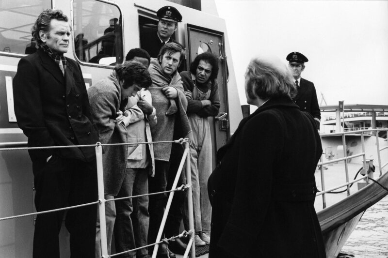 Peter Jörgensen (Christoph Quest, vorne rechts) wartet darauf, dass Kapitän Meider (Hans Heine, links) und seine geretteten Besatzungsmitglieder von Bord gehen. – Bild: NDR/​Lilo-Foto