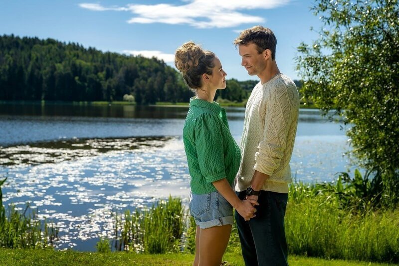 Lea (Vita Tepel) und Mik (Florian Frowein) stehen sich am grünen Ufer eines schillernden Gewässers gegenüber, und sehen sich verliebt in die Augen. – Bild: Ralf Wilschewski