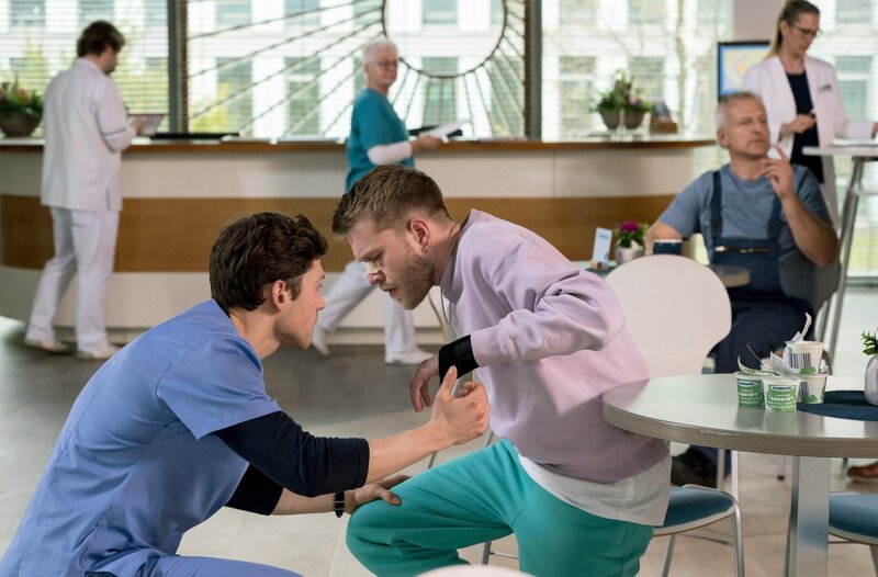 Der 25-jährige Vincent Tülke (Antonije Stankovic, r.) bekommt einen Krampfanfall. Florian Osterwald (Lion Wasczyk, l.) eilt zur Hilfe (mit Kopars:innen, h.). – Bild: ARD/​Jens-Ulrich Koch