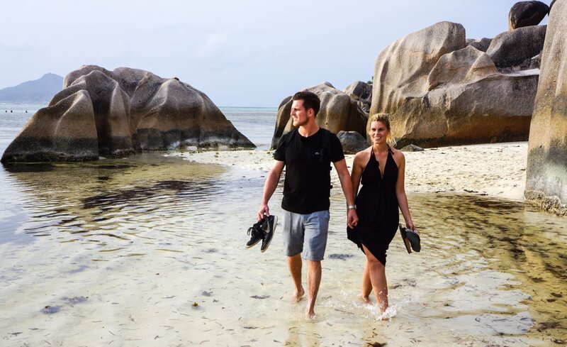 Die Passagiere – das Pärchen Scarlett Stegmann und Matthias Moritz – schlendern am Strand der Insel La Digue auf den Seychellen. – Bild: BR/​Deborah Stoeckle