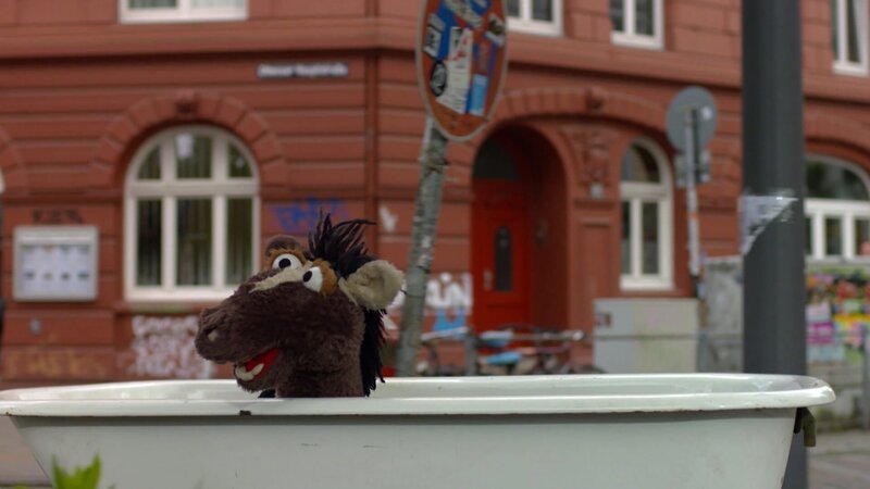 Mit seiner eingetauschten Badewanne fährt Pferd durch die Stadt. – Bild: NDR/​Sesame Workshop