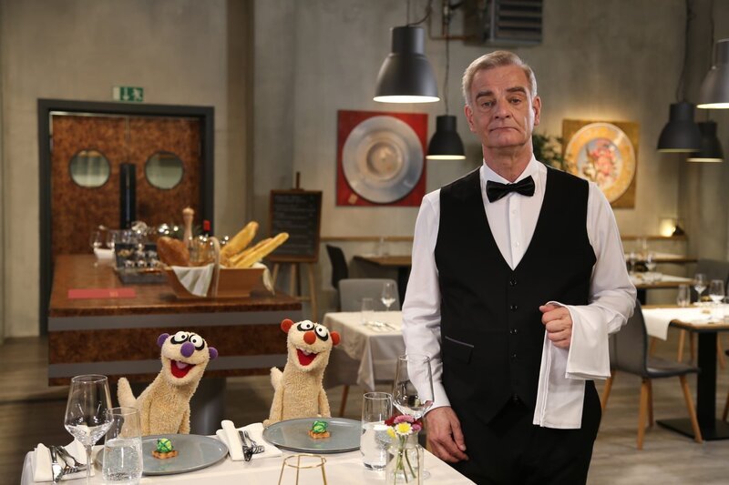 Jan und Henry recherchieren in einem Restaurant und befragen den Kellner (Heinrich Schafmeister) zum Thema „Schluckauf“. – Bild: NDR/​bigSmile