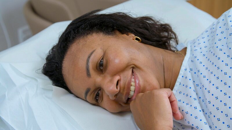Close up of Vee C smiling as she lies on clinic bed during surgery – Bild: Warner Bros. Discovery, Inc. or its subsidiaries and affiliates