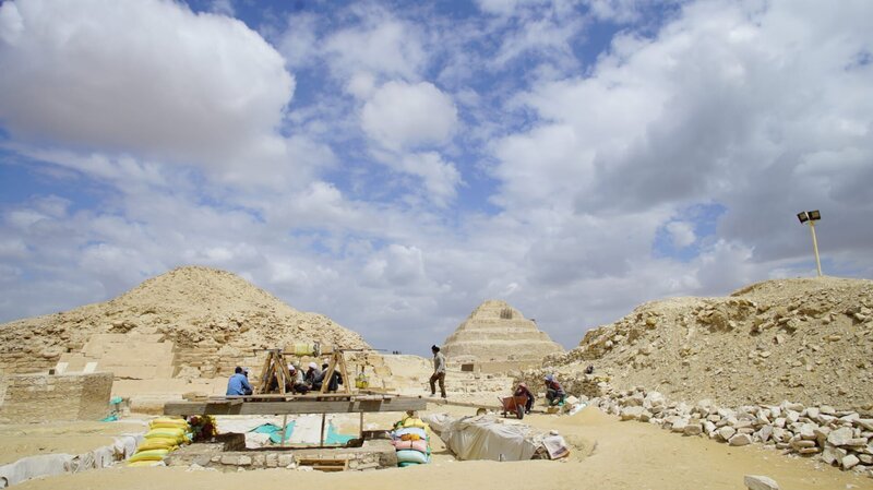 Saqqara, Ägypten – Die Mumienwerkstatt und der Gemeinschaftsgrabschacht liegen im Schatten von zwei der berühmtesten Pyramiden von Saqqara – der Stufenpyramide und der Unas-Pyramide. Arbeiter nähern sich der Winde, mit der unschätzbare Artefakte aus dem Grabschacht befördert werden. (National Geographic/​Rafael Libson-Hochenberg) – Bild: Licensed by Walt Disney Company Germany GmbH