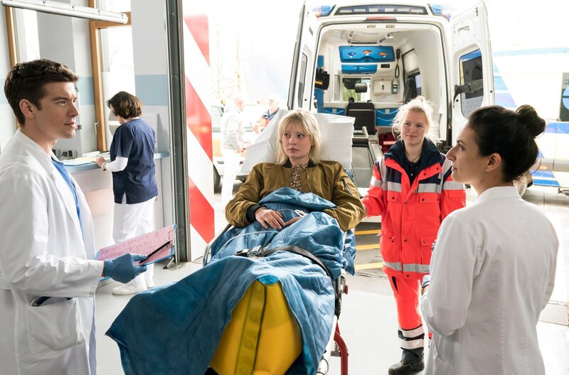 Ben Ahlbeck (Philipp Danne) und (Sanam Afrashteh, r., mit Komparsin) sind entgeistert, als Susanne Fink (Berit Vander, M.) ins Johannes-Thal-Klinikum eingeliefet wird. Susi ist die Babysitterin ihrer Tochter Raya. – Bild: ARD/​Jens-Ulrich Koch