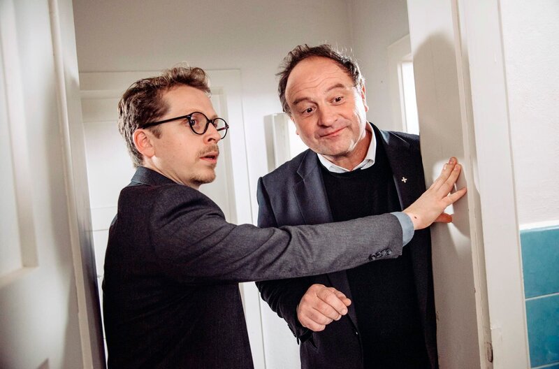 Pfarrer Brandl empfängt den Generalvikar, nachdem er den „tauchenden“ Florian im Bad übersehen hat. Von links: Pfarrer Simon Brandl (Ferndinand Schmidt-Modrow) und Generalvikar Kaiser (Pfarrer Rainer Maria Schießler). – Bild: BR/​Nadya Jakobs
