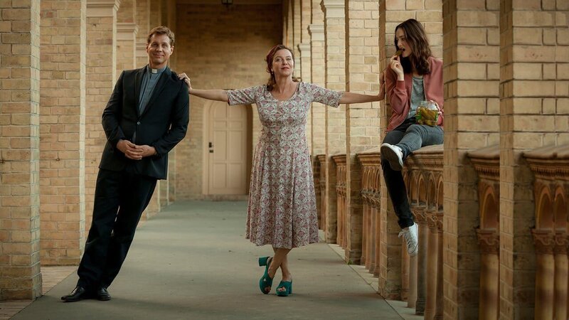 Pfarrer Benedikt (Thomas Heinze, l.) hat eine sehr eigene Art, Amelie (Margarita Broich, M.) und Lou (Maria Ehrich, r.) Trost zu spenden. Amelie lebt auf, Tochter Lou findet es befremdlich. – Bild: Romance TV