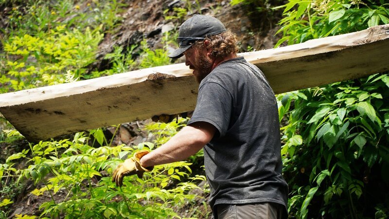 Scott Allen trägt eine Holzplanke. – Bild: Warner Bros. Discovery