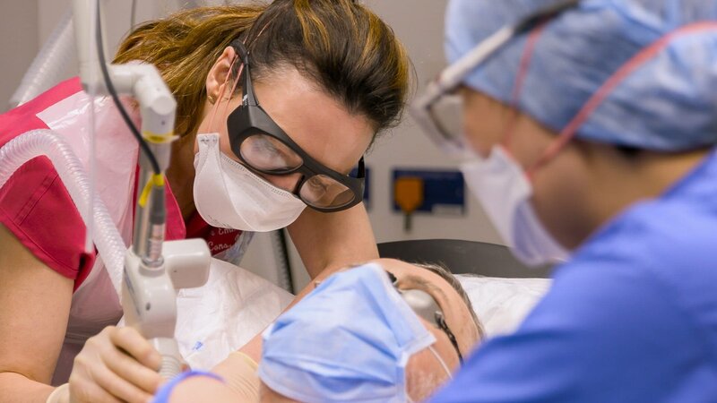 Mid shot of Dr Emma, masked up, using laser on Tony H’s chest – Bild: 2023 Warner Bros. Discovery, Inc. or its subsidiaries and affiliates.