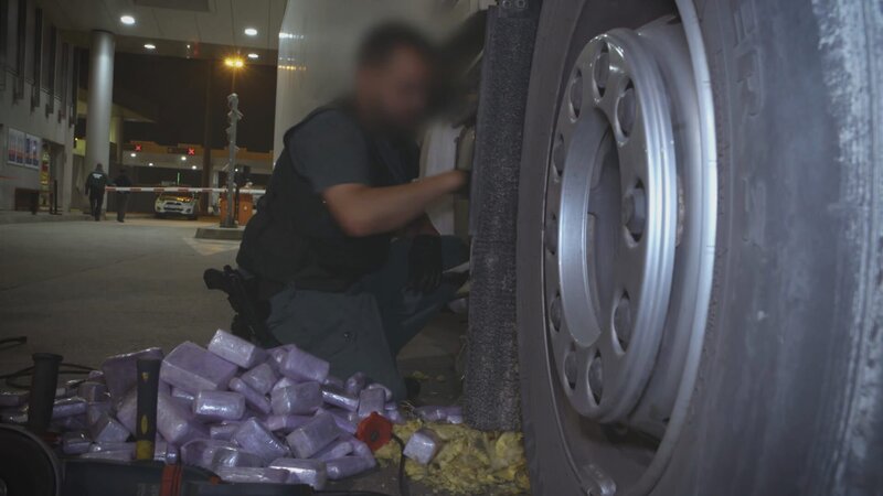 Ein Grenzbeamter entfernt versteckte Drogen aus einem Lastwagen. – Bild: Warner Bros. Discovery