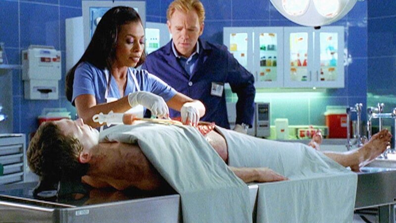 Alexx (Khandi Alexander) und Horatio (David Caruso) sehen sich den toten Jungen an, der eine Handvoll Ecstasy-Pillen geschluckt hat. Im Magen finden sie tatsächlich eine unverdaute Tablette mit einem Logo darauf, das ihnen bekannt vorkommt … – Bild: TVNOW /​ CBS