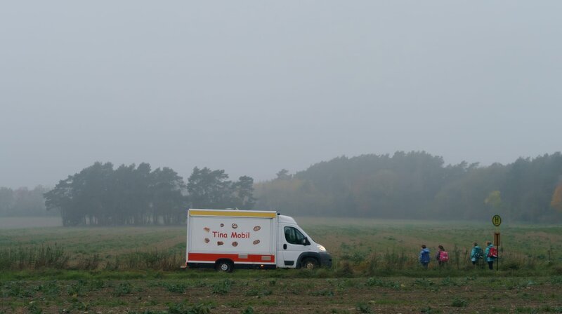„Tina mobil“ erzählt von den täglichen Problemen und Sorgen einer dreifachen Mutter in Pankow. Der Kampf ums Überleben, das mangelnde Geld – aber Tinas Maxime ist: Man kann alles schaffen, was man will. Und wenn man es nicht schafft, hat man es eben nicht genug gewollt. – Tinas Mobil fährt durchs Morgengrauen. An einer Haltestelle stehen Grundschüler und warten auf den Bus. – Bild: rbb/​ARD/​X Filme Creative Pool GmbH/​Stefan Erhard