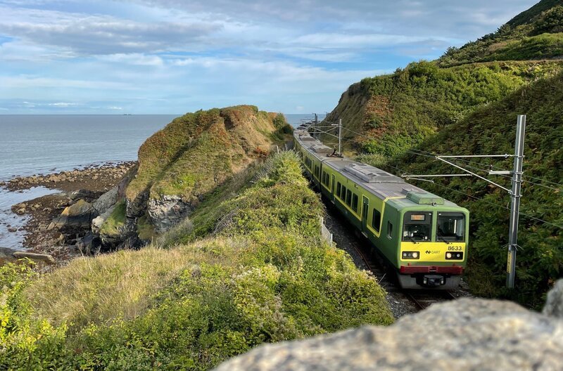 Der DART lässt die letzte Klippe hinter sich liegen: Der Nahverkehrszug zwischen Greystones und Bray fährt auf eingleisiger Strecke. Parallel zur Bahn verläuft ein Spazierweg, der Cliff Walk. – Bild: Kirsten Ruppel /​ SWR