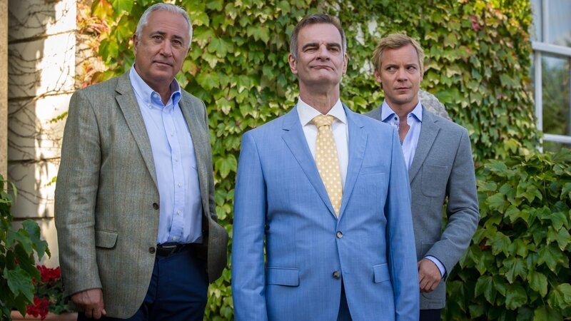 William (Robert Giggenbach, l.) hat Zweifel an der wahren Identität von Richards (Heinrich Schafmeister, M.) Stargast Johnny (Christoph von Friedl, r.) – Bild: JON AILES