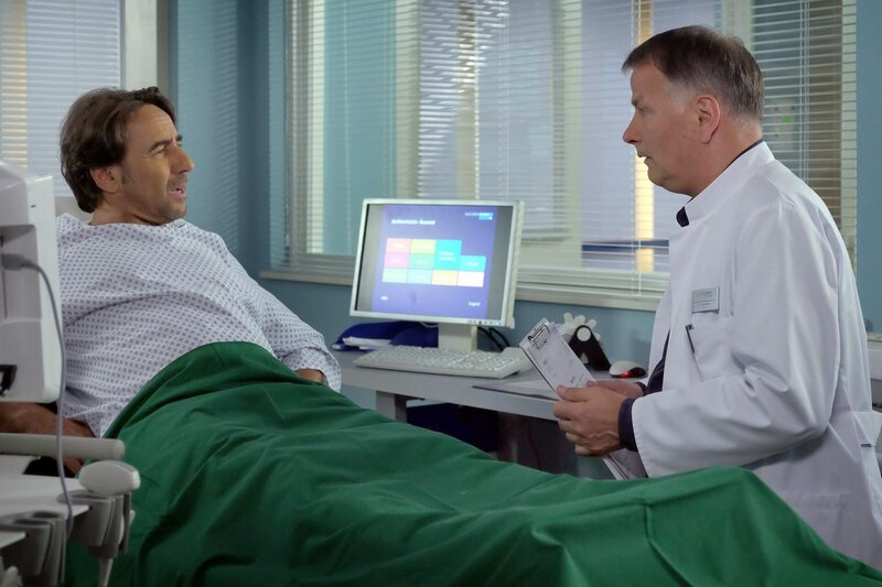 Oliver Heller (Dieter Landuris, links) kommt mit starken Bauchschmerzen in die Klinik. Er erkennt Dr. Roland Heilmann (Thomas Rühmann) sofort wieder und es stellt sich heraus, dass Oliver der Ex-Mann von Rolands neuer Flamme Kerstin Heller ist. Roland ist das ziemlich unangenehm, doch er versucht, sich nichts anmerken zu lassen. – Bild: BR/​MDR/​Saxonia Media Filmproduktions GmbH/​Sebastian Kiss