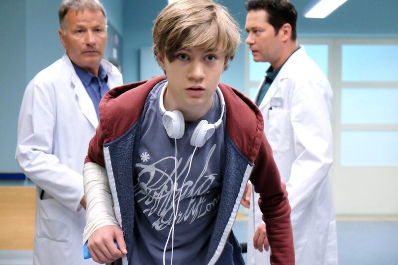 Dr. Brentano (Thomas Koch, hinten rechts) behandelt Max (Alessandro Schuster, vorn Mitte), der weder seinen vollen Namen angeben will noch eine Krankenkassen-Karte hat. Max wollte die Behandlung seiner gebrochenen Hand bar bezahlen. Klinikchef Dr. Roland Heilmann (Thomas Rühmann) erklärt Max, dass sie bei der Behandlung Minderjähriger die Eltern informieren müssen. Und wenn Max das nicht will, dann eben das Jugendamt. Diese Informationen reichen Max und er flüchtet aus der Klinik. – Bild: BR/​MDR/​Saxonia Media Filmproduktions GmbH/​Sebastian Kiss