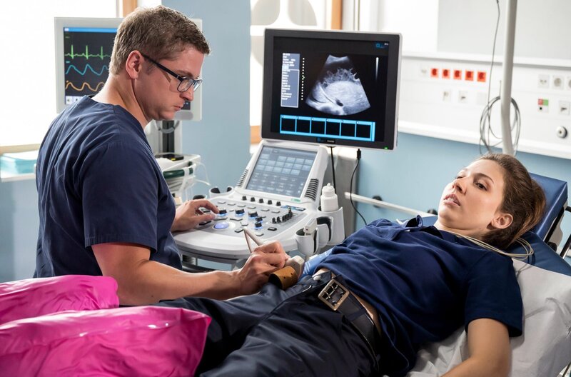 Die Rettungssanitäterin Rahel Weisskron (Amina Merai, r.) wurde vor der Notaufnahme schwer verletzt. Elias Bähr (Stefan Ruppe, l.) untersucht sie mit dem Ultraschallgerät. – Bild: ARD/​Jens-Ulrich Koch