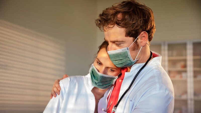 Lisa (Marie Seiser, l.) ist total erschöpft, Dr. von Hatzfeld (Tom Radisch, r.) nimmt sie in den Arm. Sie wurden von einem plötzlichen Ansturm auf die Praxis überrascht. In einem Wettrennen gegen die Zeit versuchen sie hinter die Ursache der mysteriösen Erkrankung zu kommen und die Quarantäne zu beenden. – Bild: ARD/​Christian Lüdeke
