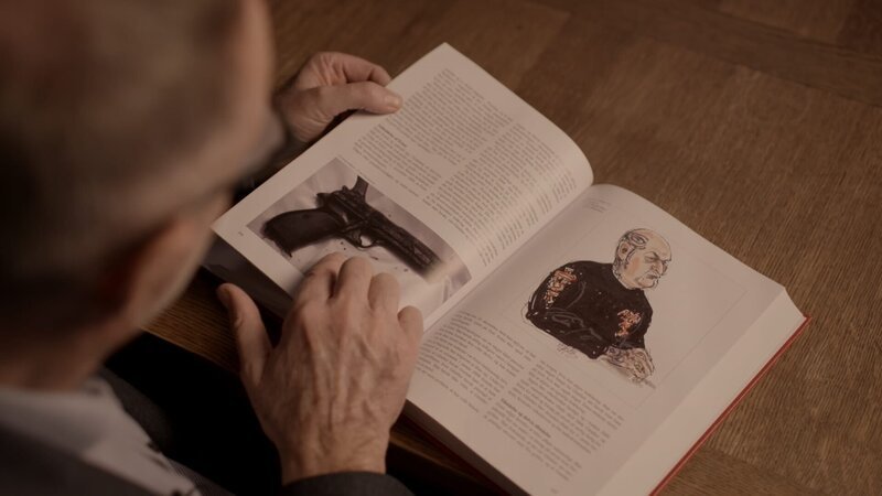 Kommissar Bent Isager-Nielsen blättert durch ein Buch, das die größten Kriminalfälle der skandinavischen Geschichte behandelt. Darunter auch der Fall zum ermordeten Nhut. Die Pistole aus dem Fall ist durch die jahrelange Lagerung im Wasser komplett verrostet. – Bild: ZDF