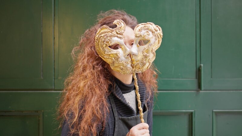 Marilisa Dal Cason mit einer goldenen Stab-Maske, mit der man sich kenntlich oder unkenntlich mit einer kleinen Handbewegung machen kann. – Bild: BR Marilisa Dal Cason mit einer goldenen Stab-Maske, mit der man sich kenntlich oder unkenntlich mit einer kleinen Handbewegung machen kann. – Bild: BR
