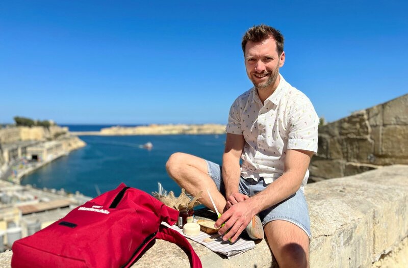 Moderator Daniel Aßmann bei einem kleinen Picknick mit maltesischen Spezialitäten und Blick auf den Hafen von Valletta. – Bild: WDR/​Antje Wunsch-Baumgarten