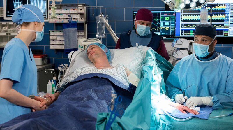 Im OP liegt Beat (Roland Bonjour, v.M. mit Komparse, h.) und wird von Matteo (Mike Adler, r.) und seiner Frau Elly (Juliane Fisch, l.) operiert. – Bild: ARD/​Jens-Ulrich Koch