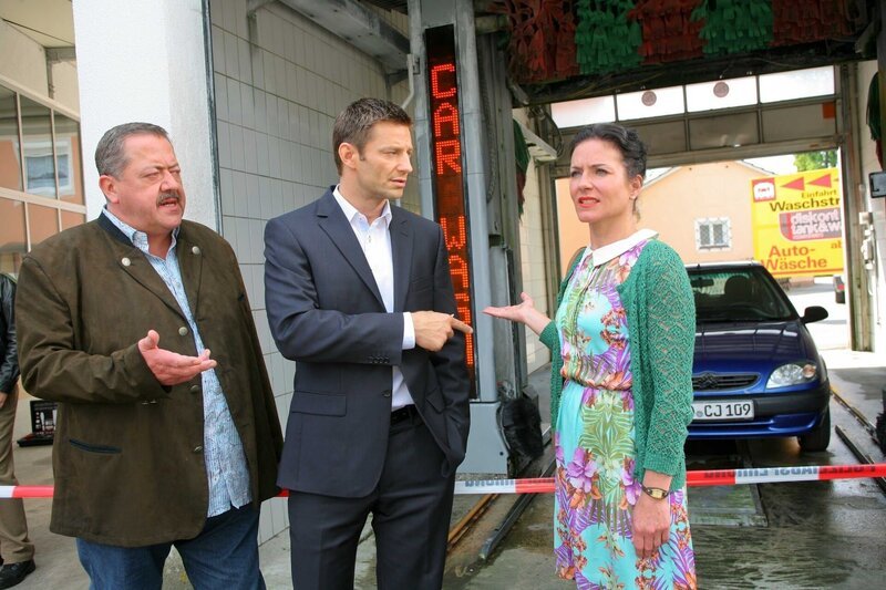 Mord in der Waschstraße: Nachdem Sekretärin Stockl (Marisa Burger, r.) eine Leiche entdeckt hat, informiert sie die Kollegen Hansen (Igor Jeftic, m.) und Hofer (Joseph Hannesschläger, l.). – Bild: ZDF/​Christian A. Rieger