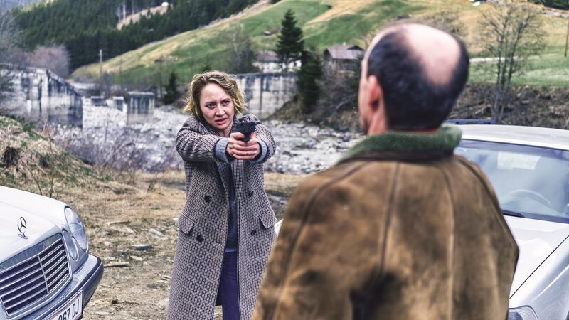 Blum (Anna Maria Mühe) bedroht Sebastian Hackspiel (Gerhard Liebmann) mit einer Waffe und will sein vermeintliches Brandmal sehen. – Bild: ORF/​Mona Film/​ Barry Films/​Stephan Burchardt