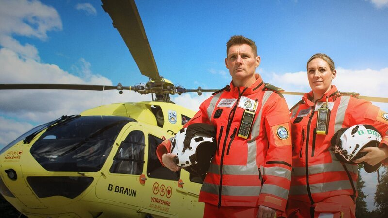 zwei Personen stehen neben einem Hubschrauber auf dem Boden – Bild: Really /​ UK Creatives /​ Warner Bros. Discovery, Inc. or its subsidiaries and affiliates
