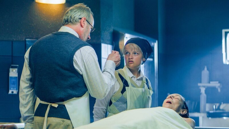 Rückblick in Blums Vergangenheit: Blums Vater Hagen (Wolfram Koch) will, dass die junge Blum (Amelie Rohde) am Leichnam einer alten Dame (Beatrice Frey) eine Kieferligatur durchführt. – Bild: ORF/​Mona Film/​ Barry Films/​Stephan Burchardt