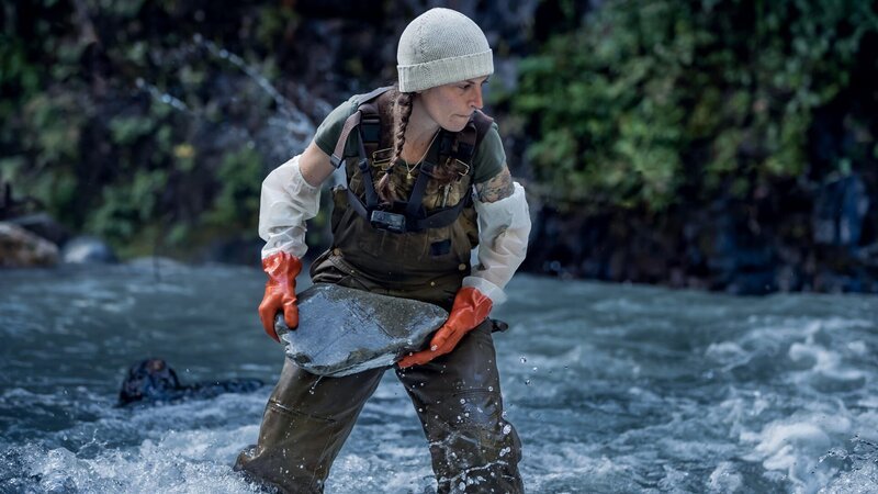 Kayla Johanson mit Schutzhandschuhen beim Steinwurf im Bach – Bild: Discovery, Inc.