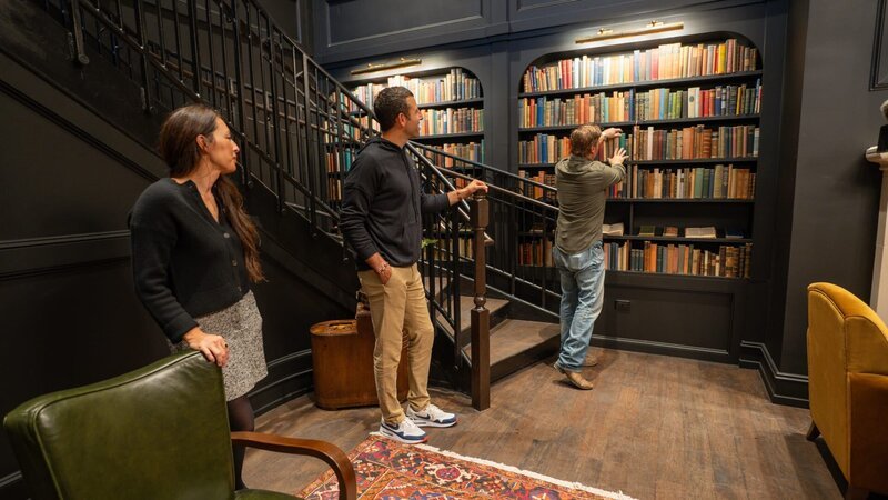 Chip, Jo, and Ben talk in the library as seen on episode 106 of Fixer Upper: Hotel. – Bild: HGTV /​ Webdam: MNRG106_HOTEL_106_STILL_ /​ Warner Bros. Discovery, Inc. or its subsidiaries and affiliates.