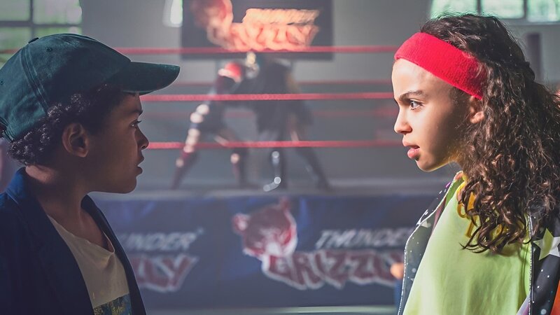 Maxi (Kiana Ben Attou, re.) und Karl (Lance Gernot Simon) überlegen, wie sie an das nächste Kartenstück kommen. Dafür müssen sie an dem Wrestler Tony Hoppe vorbei. – Bild: mdr/​Saxonia Media/​Thomas Dietze