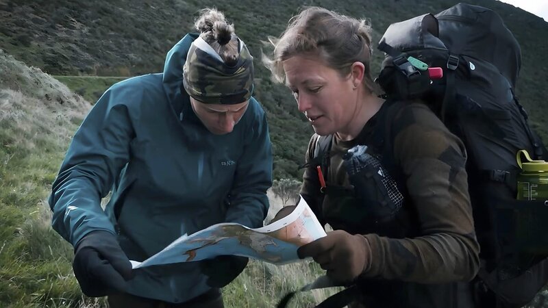 Zwei Personen überprüfen die Karte in einem Berggebiet. – Bild: Warner Bros. Discovery