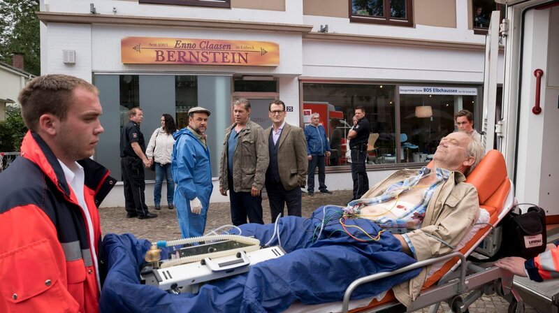 Ein brutaler Überfall auf ein Bernstein-Schmuckgeschäft in Scharbeutz: Weil der Bernsteinschleifer Enno Claasen (Hans-Heinrich Hardt, r.) ungeplant früher vom Strand zurückkommt, überrascht er zwei Einbrecher auf frischer Tat und wird dabei von einem Schuss lebensgefährlich verletzt. Finn Kiesewetter (Sven Martinek, M.), Lars Englen (Ingo Naujoks, 2.v.r.) und Dr. Henning Strahl (Christoph Tomanek, 4.v.r.) ermitteln. – Bild: ARD/​Georges Pauly