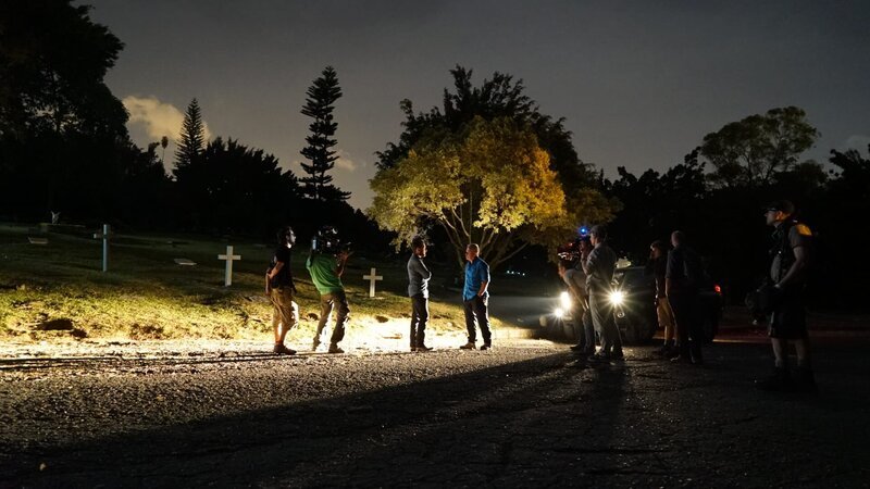 Doug Laux hält ein geheimes Treffen mit Popeye in einem Friedhof bei Nacht ab. Ein Kamerateam umgibt die beiden, beleuchtet von den Scheinwerfern von Popeyes riesigem Truck. – Bild: Discovery Channel /​ Discovery Communications