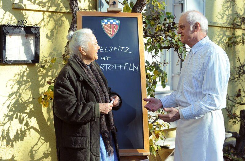 Vor dem Brunnerwirt erklärt Joseph (Michael Vogtmann) seiner Mutter Theresa (Ursula Erber), dass er möchte, dass sie kürzertritt. Weiteres Bildmaterial finden Sie unter www.br-foto.de. – Bild: BR/​Marco Orlando Pichler