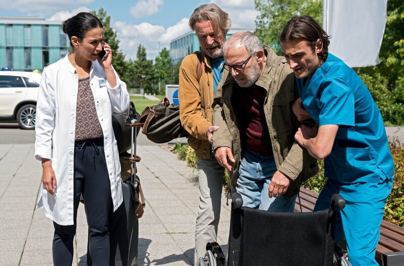 Michael Wolff (Max Volkert Martens, 2.v.l.) bringt seinen Kumpel Johann Wiesweg (Hans Klima, 2.v.r.) ins JTK. Dr. Sherbaz (Sanam Afrashteh, l.) und Ivo Maric (Jakob D’Aprile, r.) kümmern sich um den 70-jährigen. – Bild: ARD/​Jens-Ulrich Koch