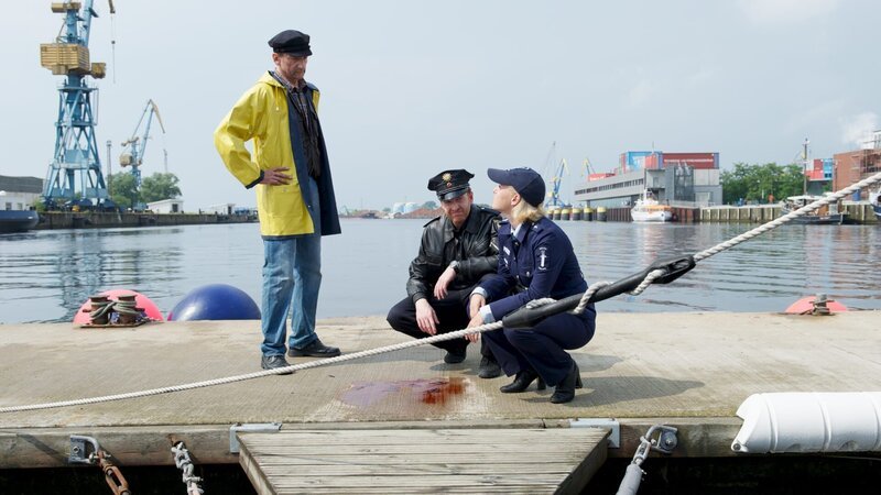 Hafenmeister Jansen (Bernd Gajkowski, l.) hat am Pier eine Blutlache und ausgeschlagene Zähne gefunden. Am Vorabend ist er genau an dieser Stelle auf einen Streit aufmerksam geworden. Ein Unbekannter hat Richter Naumann, dessen Boot hier liegt, bedroht. Die Polizisten Kai Timmermann (Mathias Junge, M.) und Leena Virtanen (Li Hagman, r.) untersuchen den Tatort. – Bild: ZDF und Marc Meyerbröker