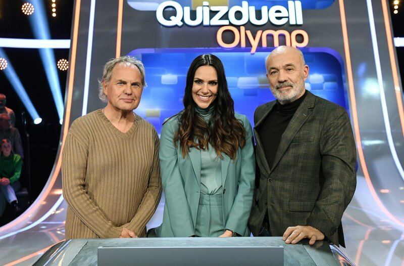 Quizmasterin Esther Sedlaczek (M.) mit den Kandidaten des Teams „Männer“: Uwe Ochsenknecht (l.) und Heiner Lauterbach (r.), beide Schauspieler. – Bild: ARD/​Uwe Ernst
