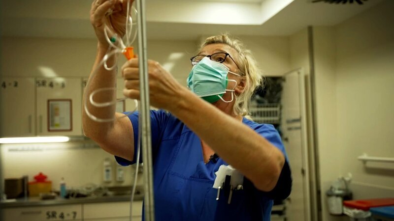 Eine Krankenschwester bereitet eine Infusion für einen Patienten vor. – Bild: Warner Bros. Discovery