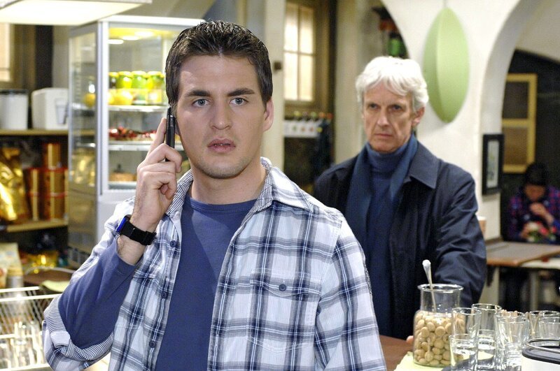 Als Lily Lars (Alexander Klaws, l.) telefonisch vorwarnen will, ist es bereits zu spät – Robert (Mathieu Carrière, r.) steht im Coffeeshop. – Bild: SAT.1 /​ Oliver Ziebe