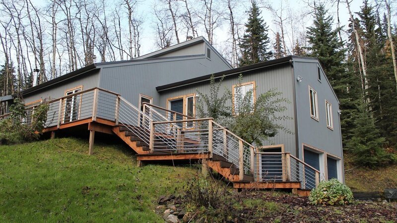 Exterior of house from driveway, shot of stairs leading to the front door, grey wood paneling with blue garage doors, on one of the stops in the Hunt family house search, Chena Forrest Drive, Fairbanks, Alaska. – Bild: Great American Country/​Scripps Networks, LLC.